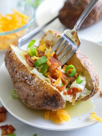 Vertical image of Air Fryer Baked Potato with toppings on a plate and a fork digging in