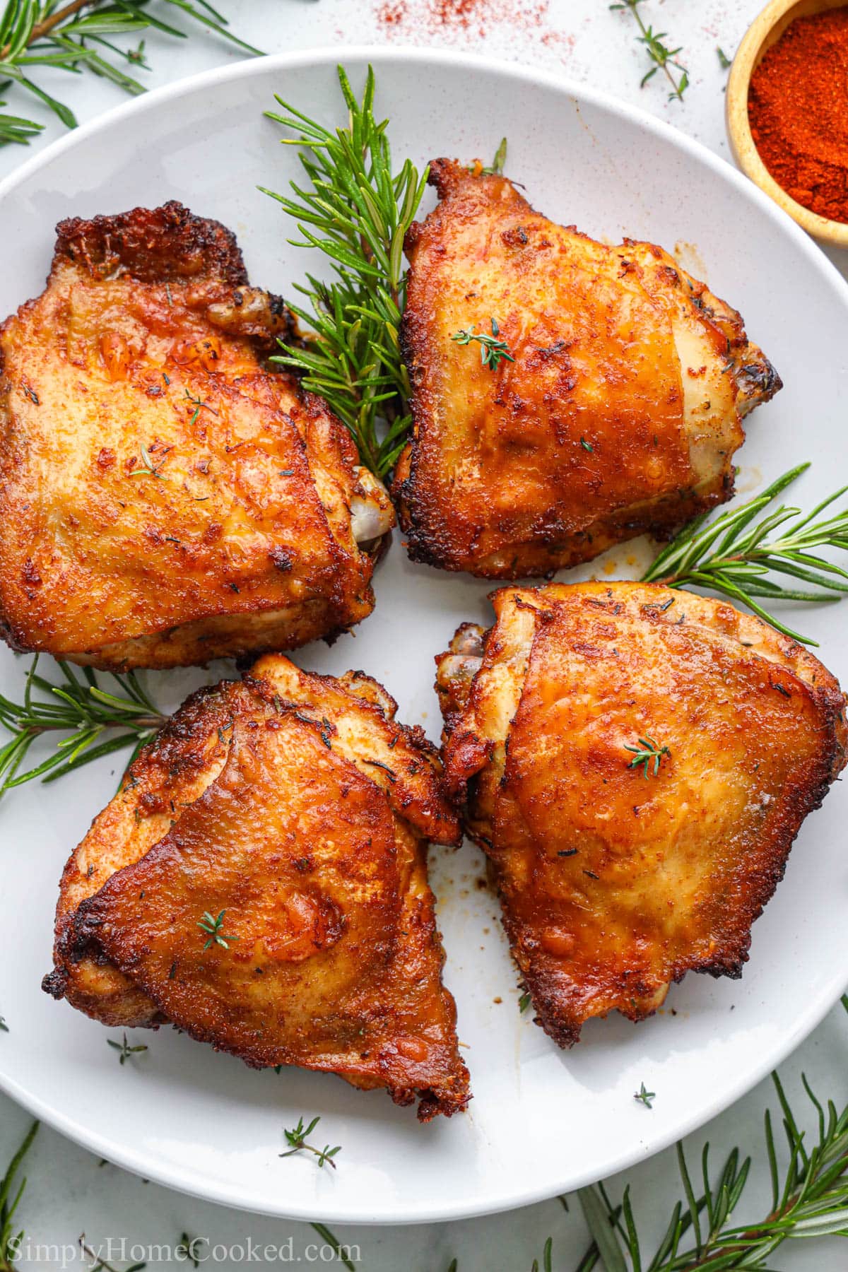 Air Fryer Chicken Thighs on a white plate with rosemary sprigs. 
