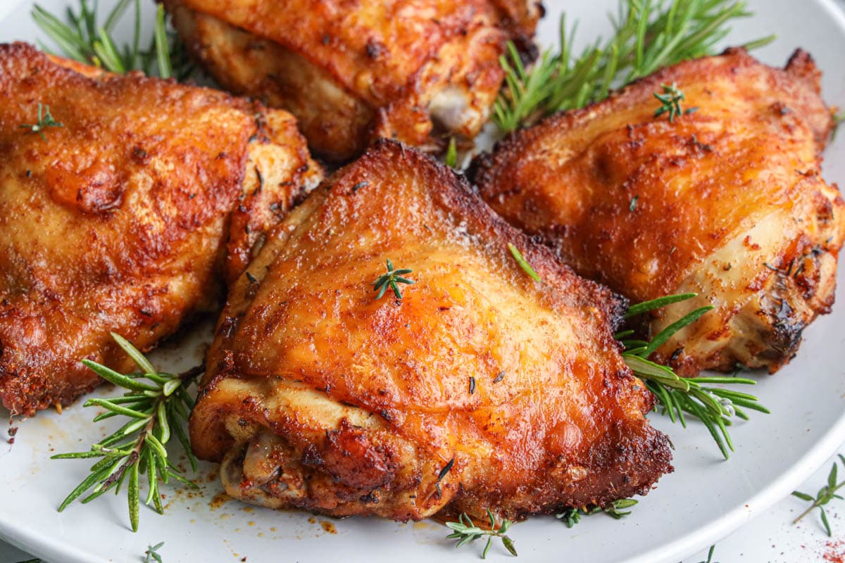 Horizontal image of Air Fryer Chicken Thighs on a white plate with rosemary sprigs.