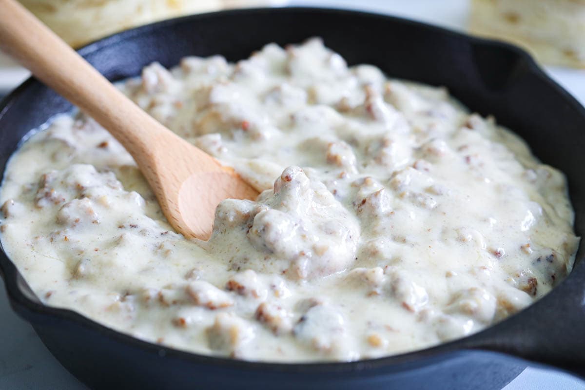 Horizontal image of Sausage Gravy being stirred in a cast iron skillet
