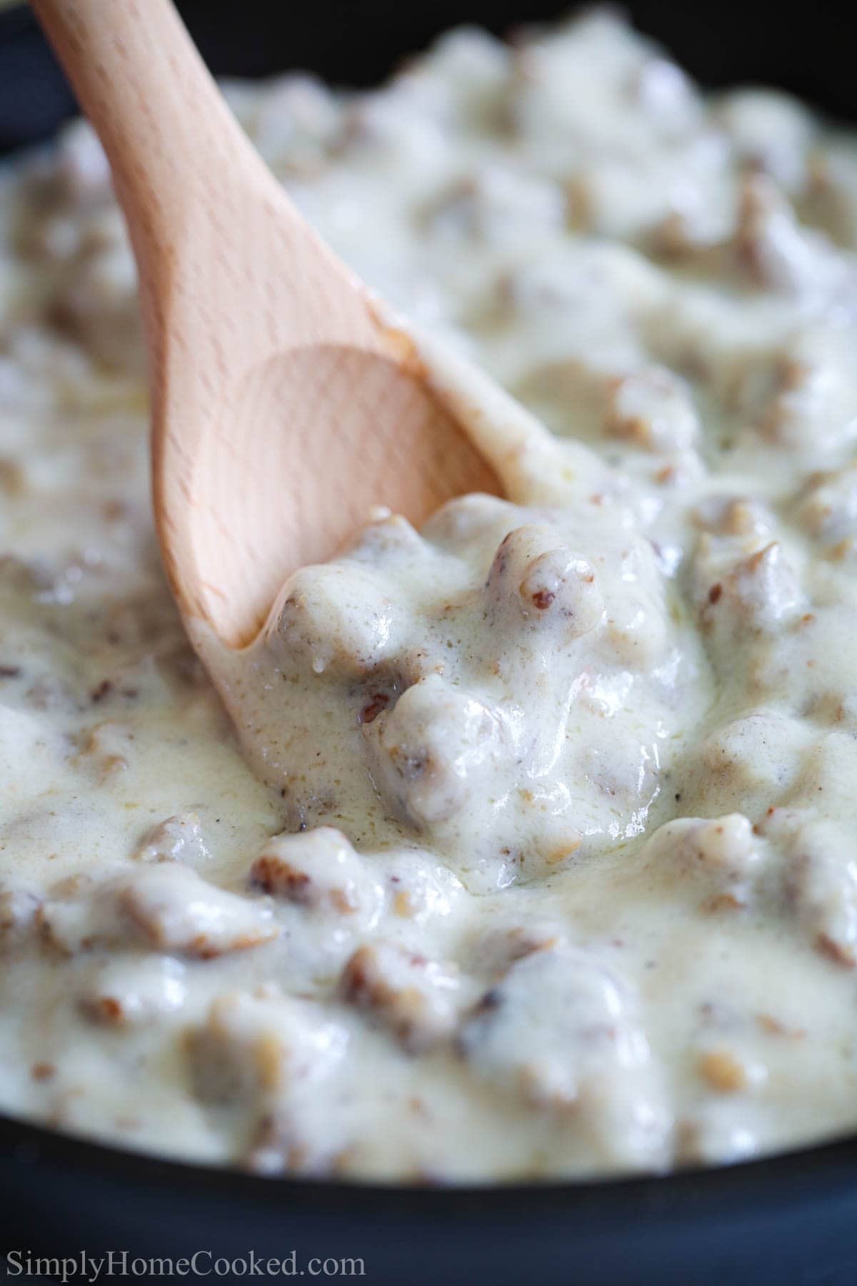 Vertical close up image of Sausage Gravy on a wooden spoon