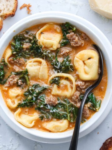 Vertical image of a bowl of Tortellini Soup with a spoon