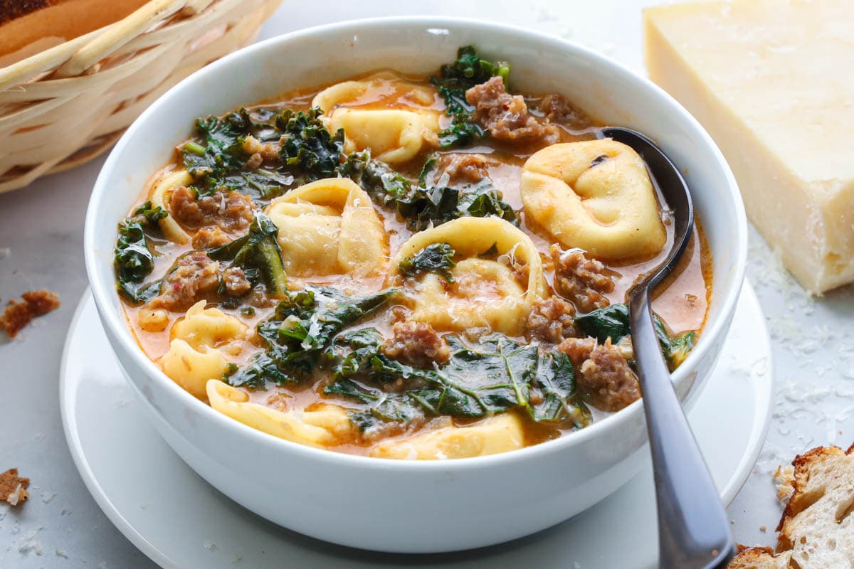 Horizontal image of a bowl of Tortellini Soup with cheese and bread nearby