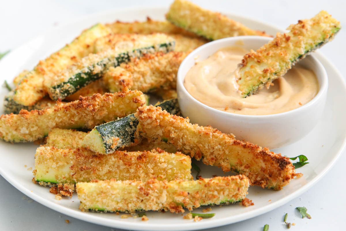 Air Fryer Zucchini Fries on a white plate with one in the dipping sauce