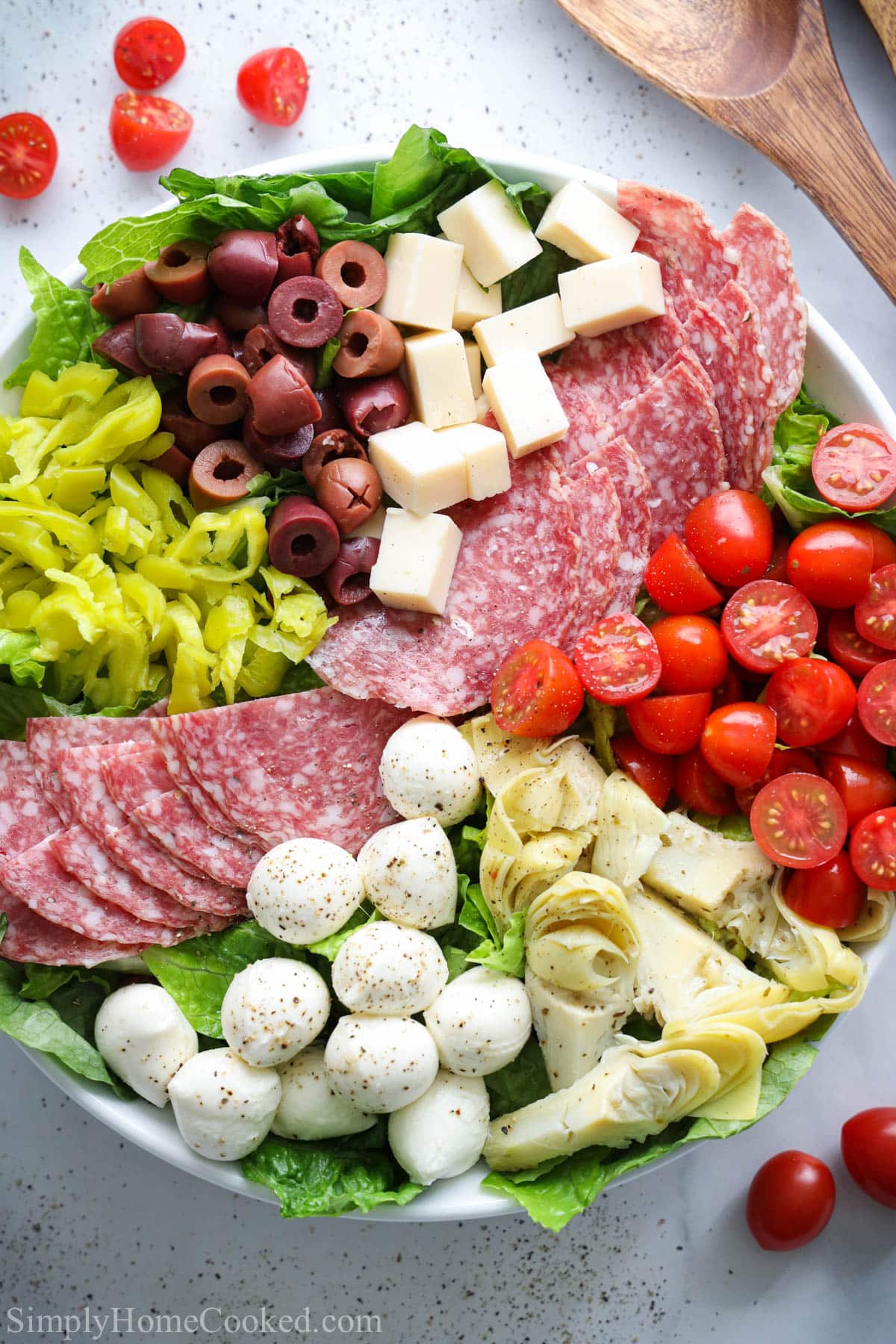 image of Antipasto Salad in a white plate with a wooden spoon next to it