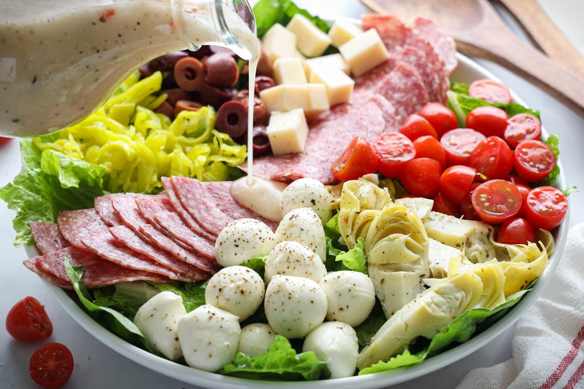 Horizontal image of Antipasto Salad with dressing being drizzled over it