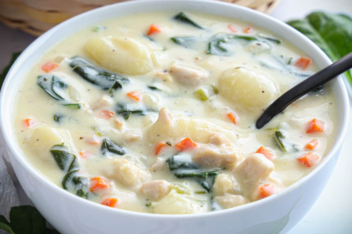 Horizontal image of a bowl of Chicken Gnocchi Soup with a spoon in it.