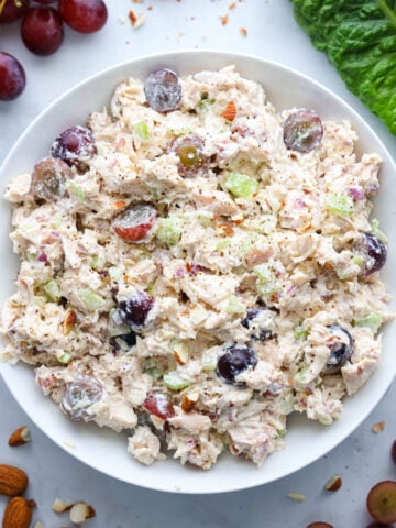 Vertical overhead image of Chicken Salad with Grapes in a white bowl with grapes and lettuce nearby