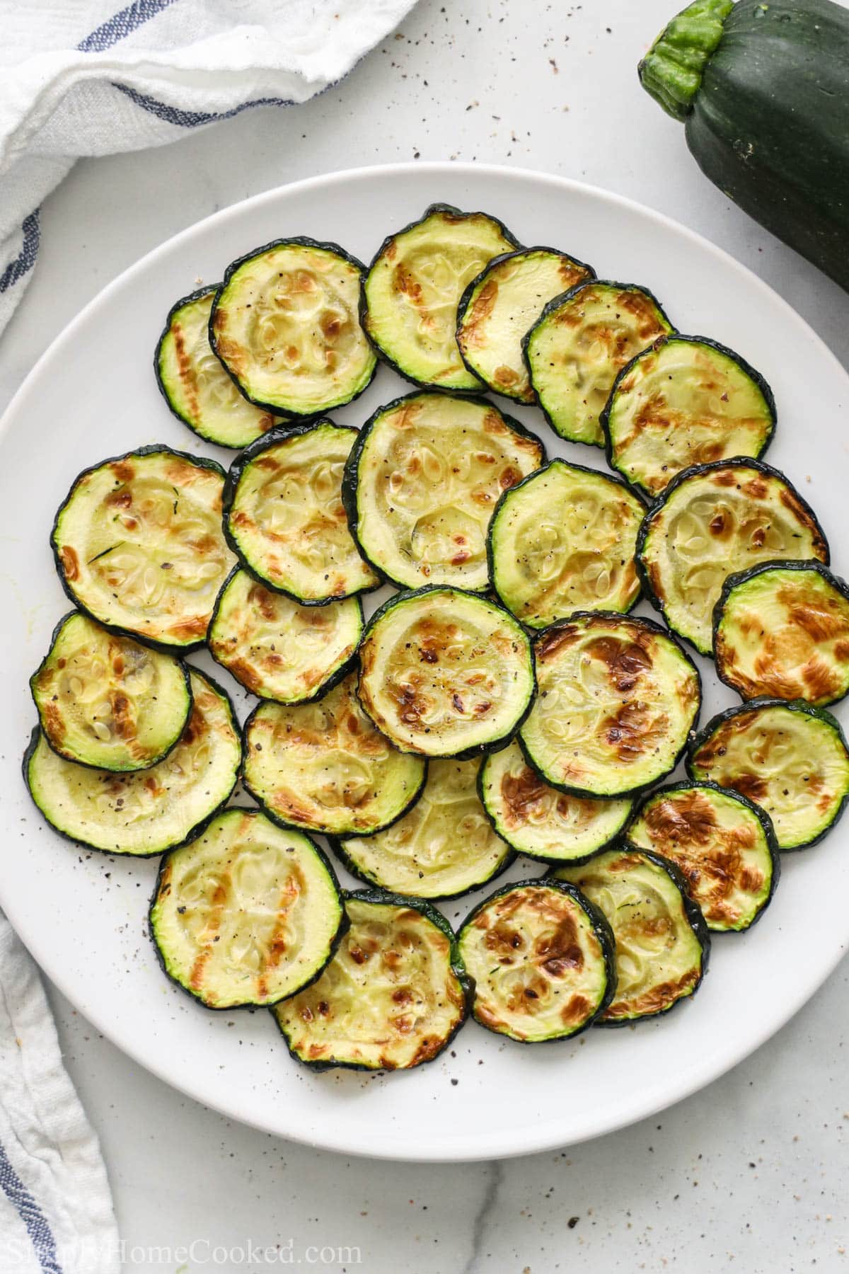 Air Fryer Zucchini layered on a white plate with a zucchini nearby