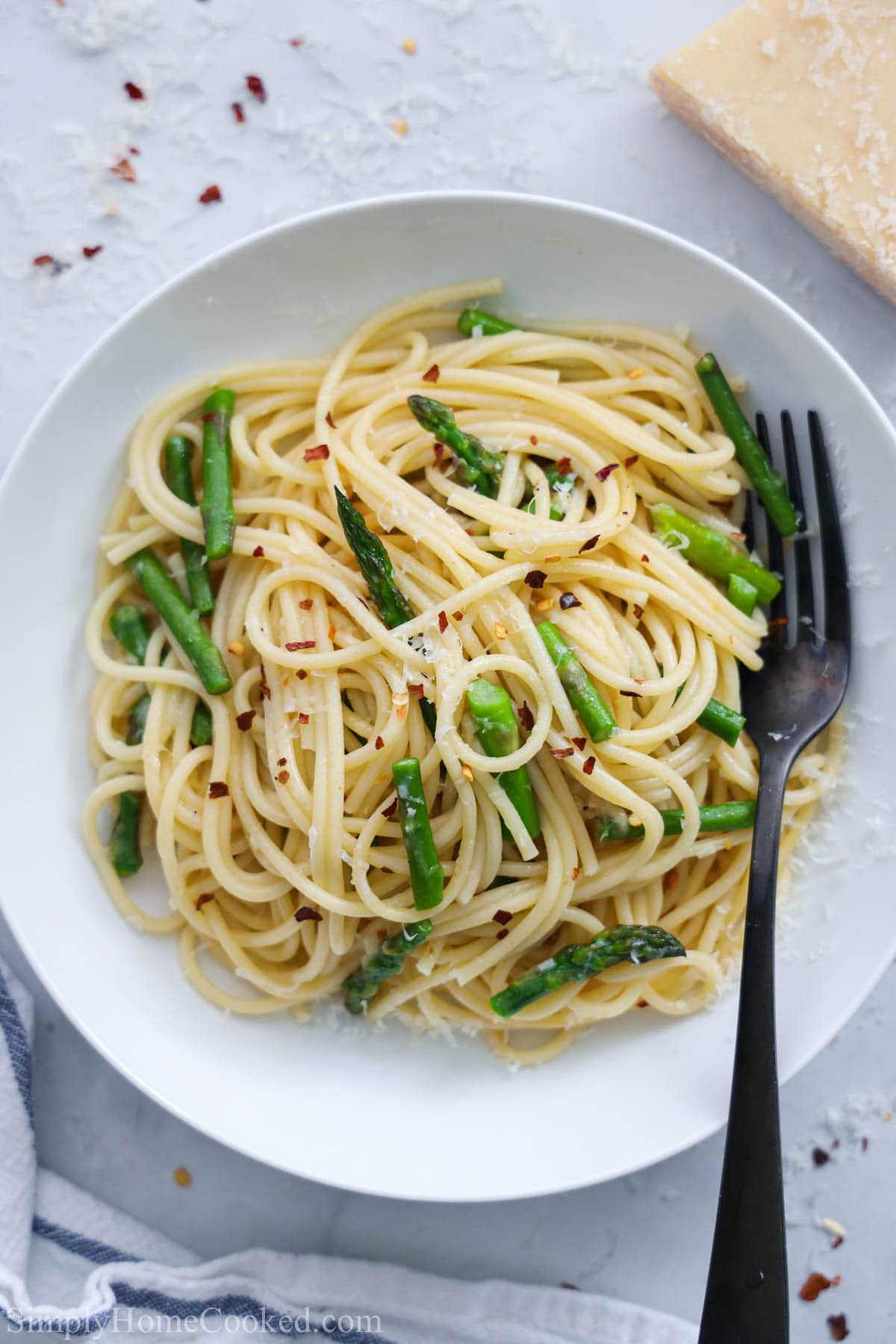 Asparagus Pasta on a white plate with a fork and Parmesan cheese nearby