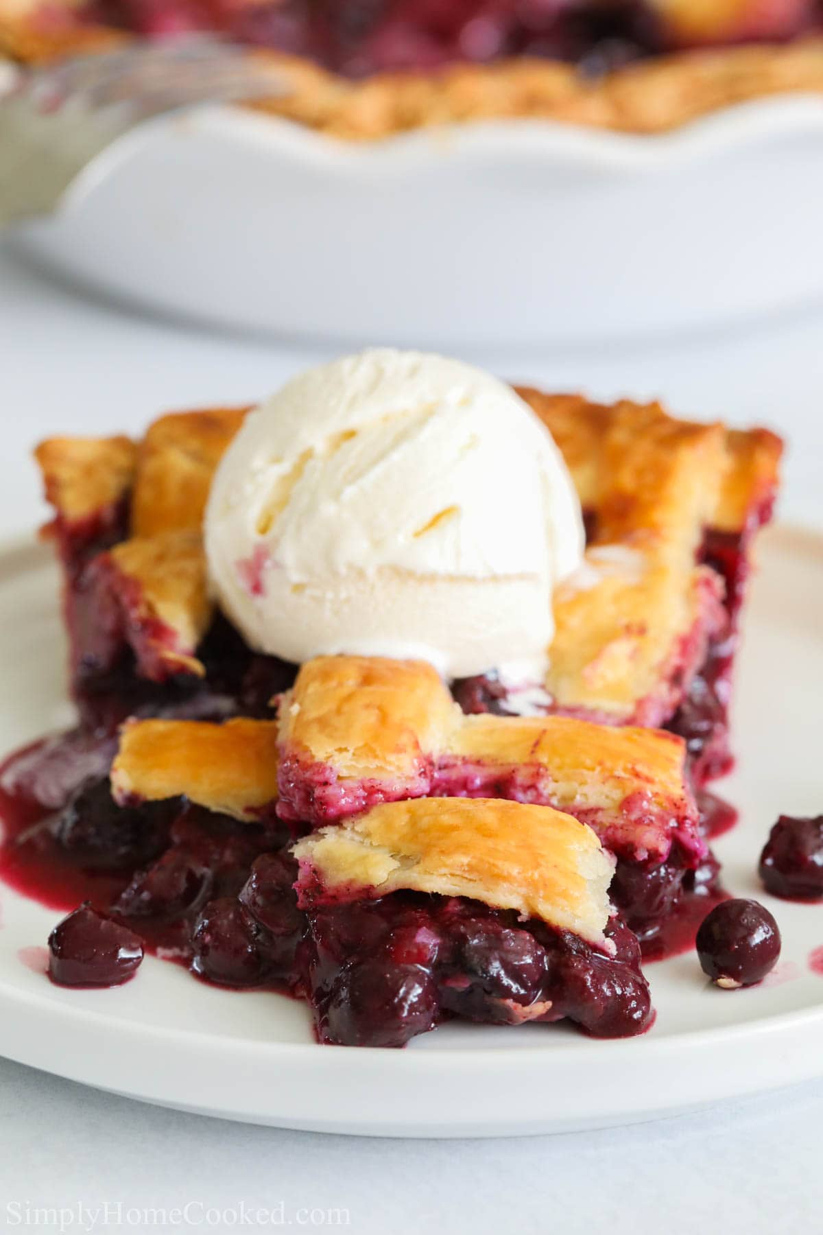 Blueberry Pie slice with a scoop of vanilla ice cream on top on a white plate