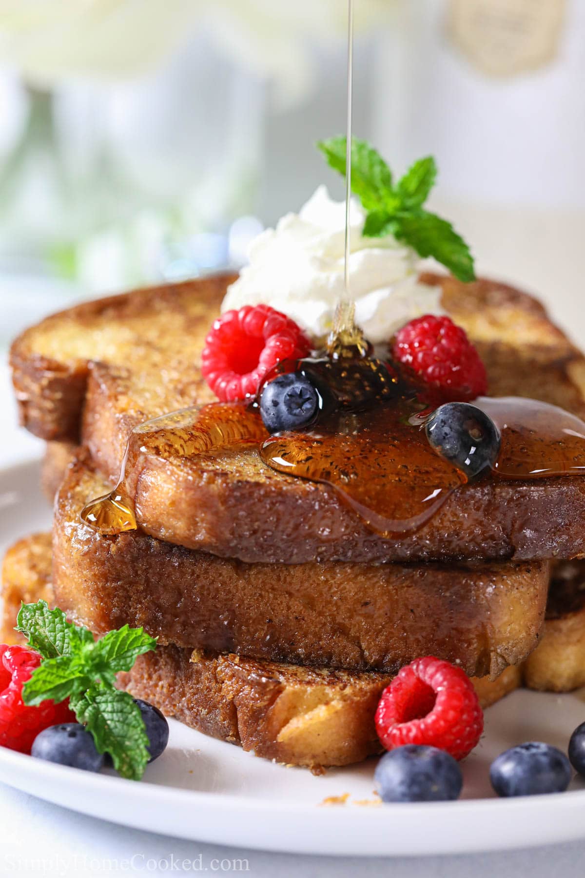 Syrup drizzling on a stack of Brioche French Toast on a plate with fresh berries and whipped cream