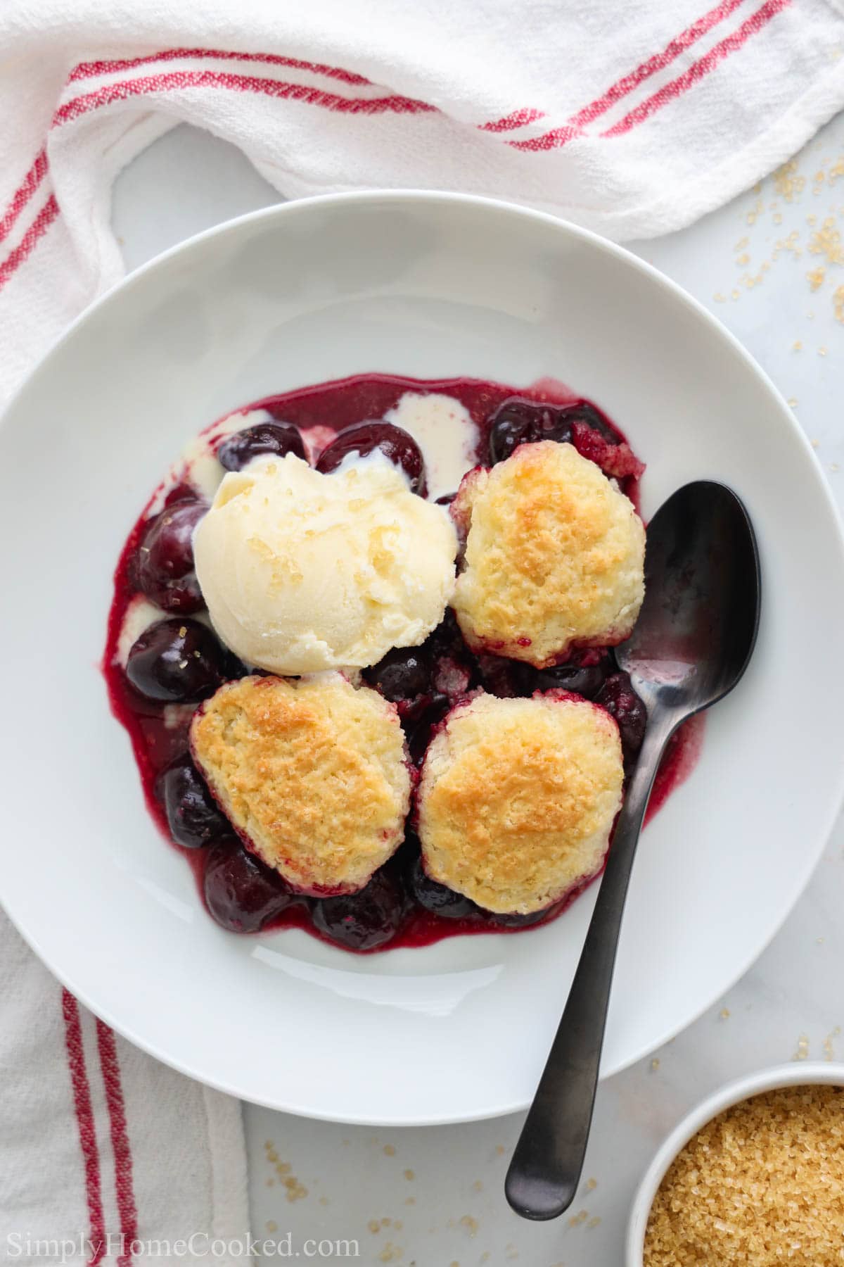 Cherry Cobbler on a white plate with a spoon and ice cream on top