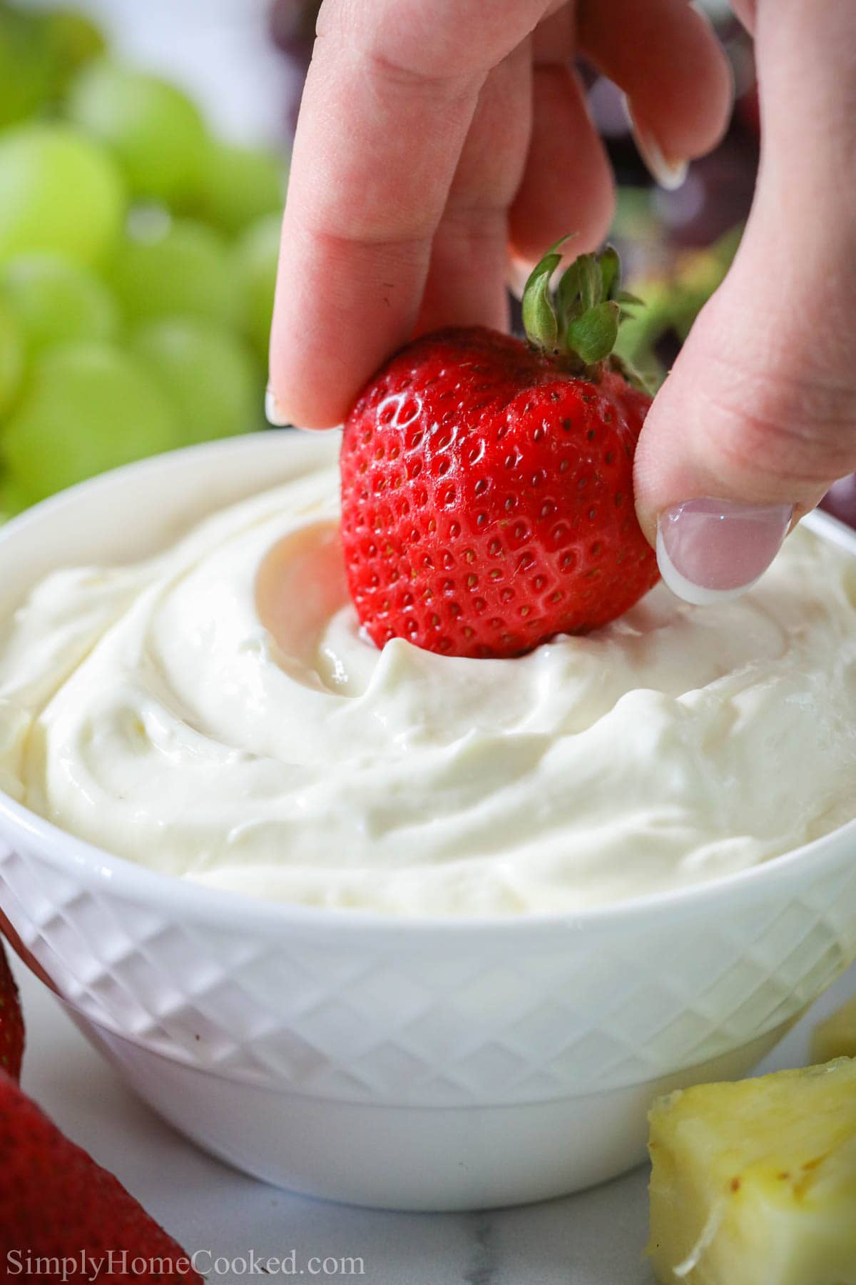 Hand dipping a strawberry into Cream Cheese Fruit Dip in a white bowl