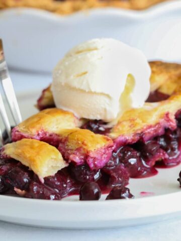 Blueberry Pie slice with a scoop of vanilla ice cream on top on a white plate with a fork