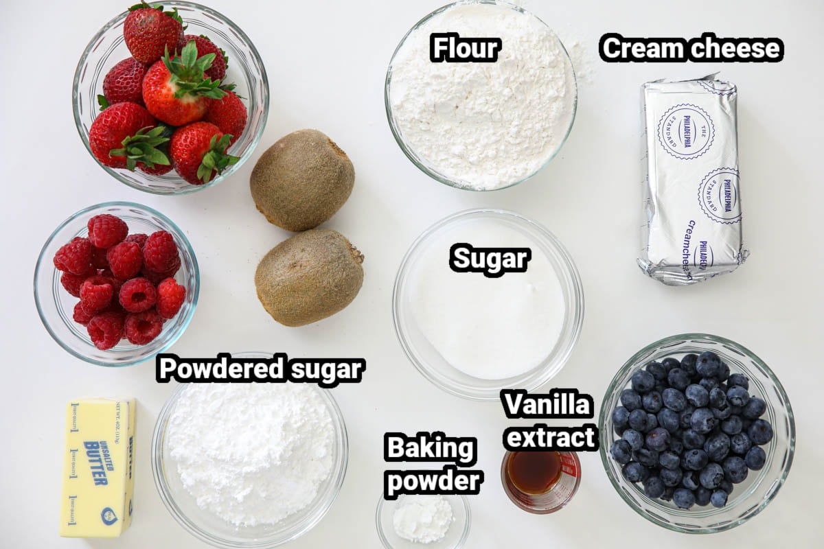 Ingredients for Fruit Pizza, including flour, sugar, cream cheese, powdered sugar, vanilla, baking powder, butter, raspberries, blueberries, strawberries, and kiwis.