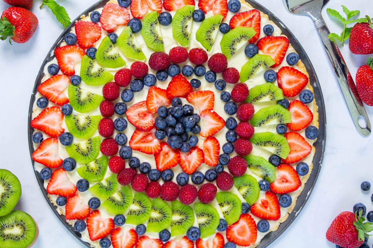 Overhead view of Fruit Pizza with strawberries and kiwis nearby