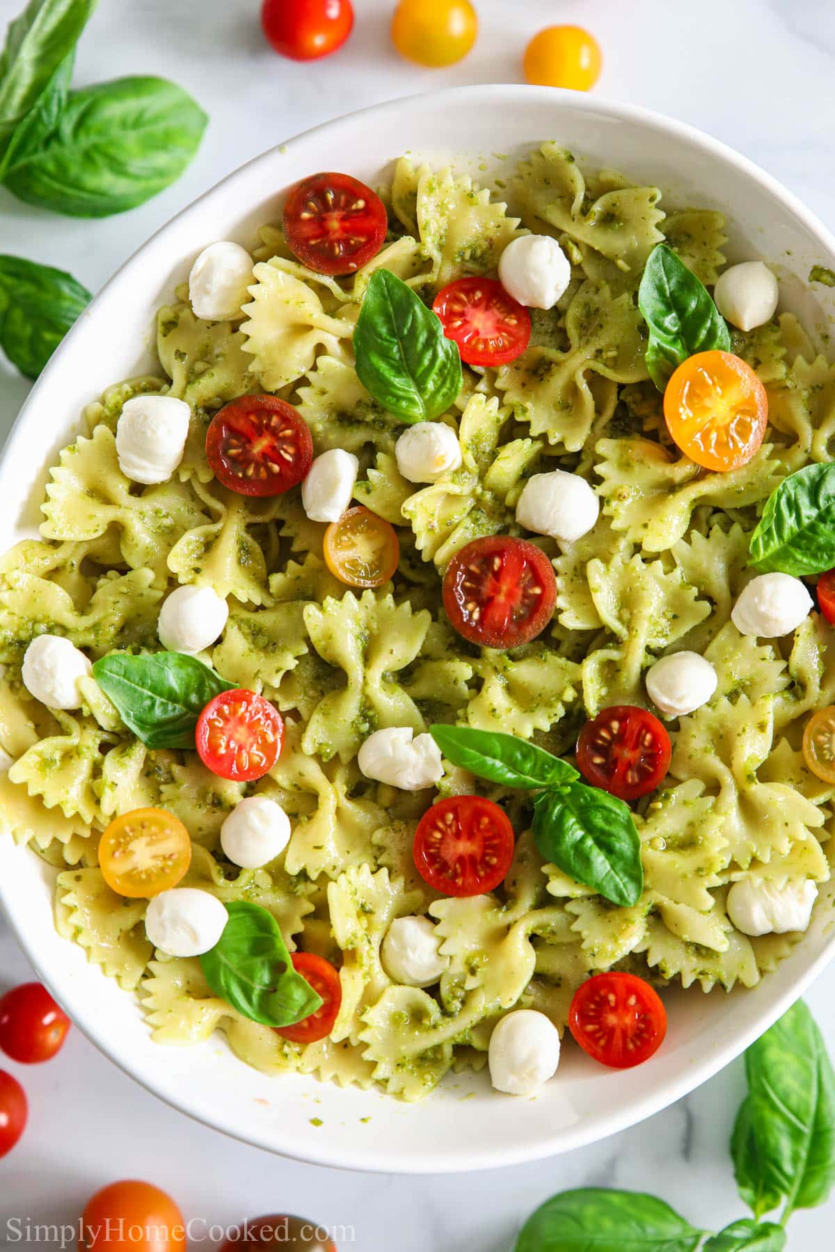 Pesto Pasta Salad on a white plate with basil and tomatoes nearby
