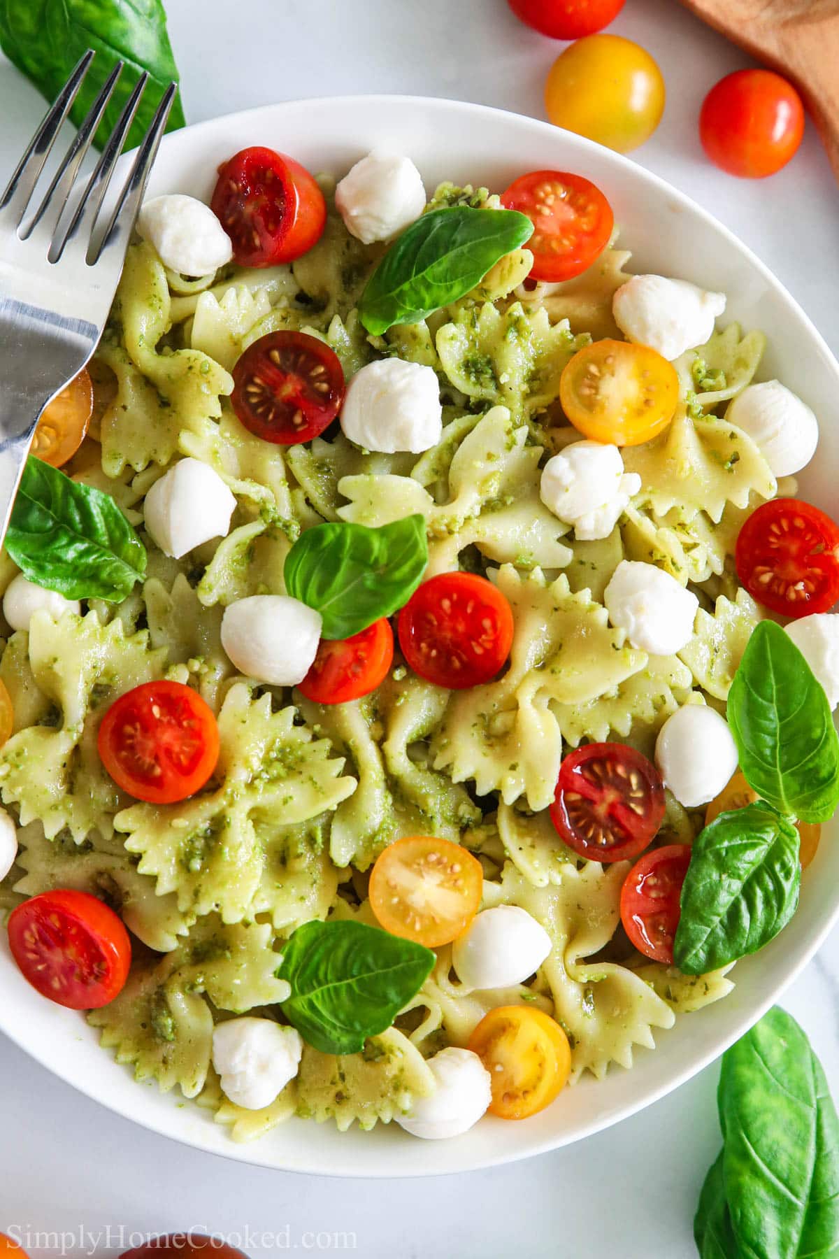 Pesto Pasta Salad on a white plate with a fork and tomatoes nearby