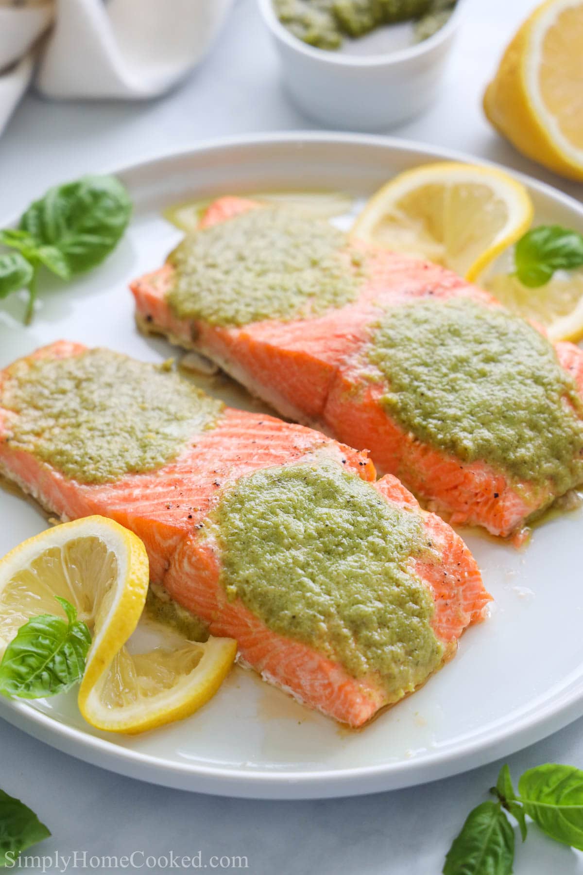 Closeup of Pesto Salmon filets on a white plate with basil and lemon slices