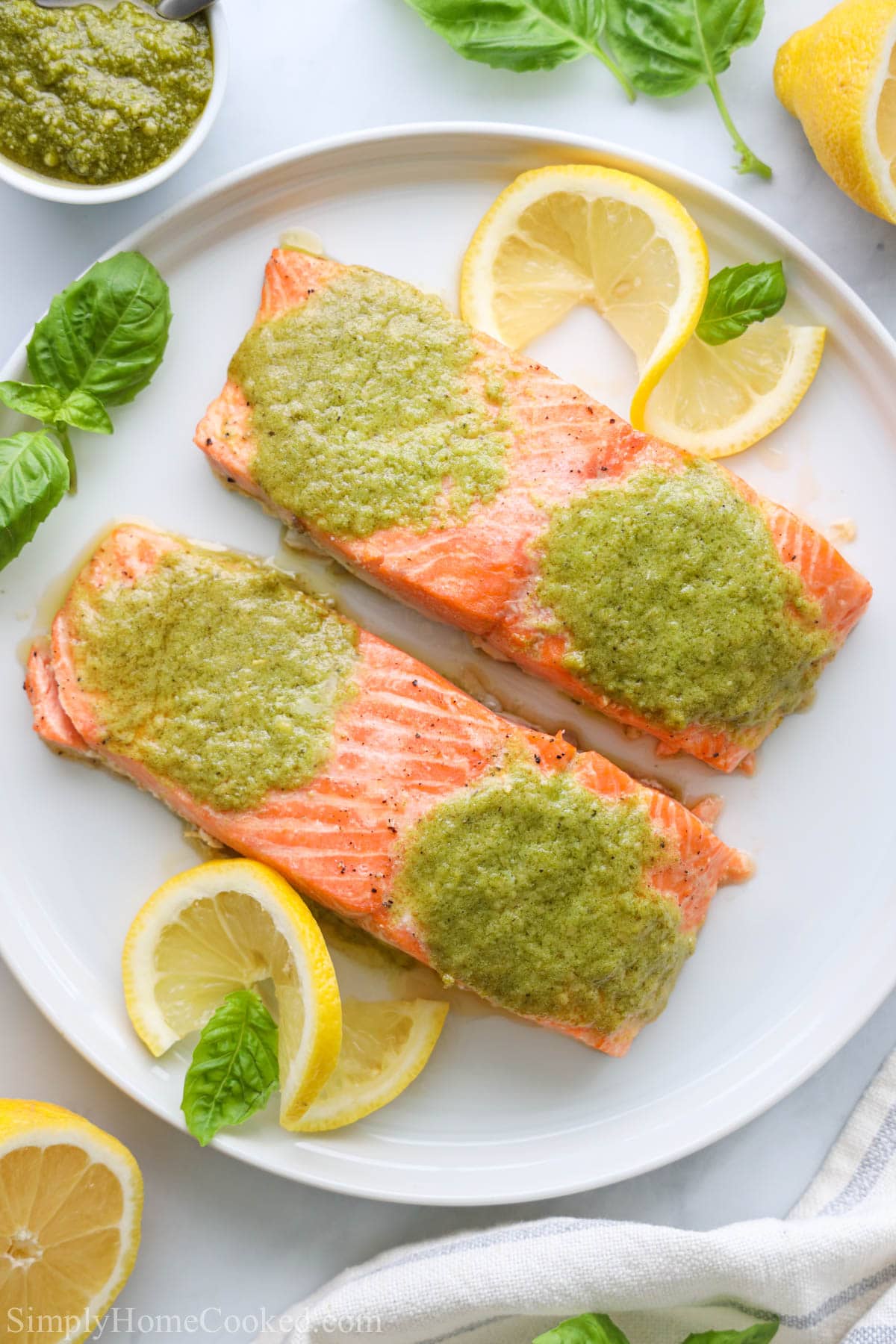 Pesto Salmon filets on a white plate with basil and lemon slices