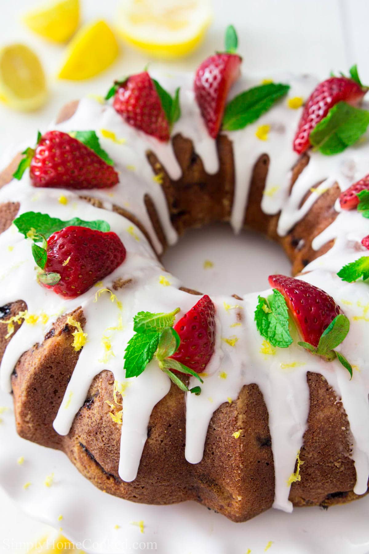 Strawberry Bundt Cake with glaze and strawberries on top with mint leaves and lemons nearby