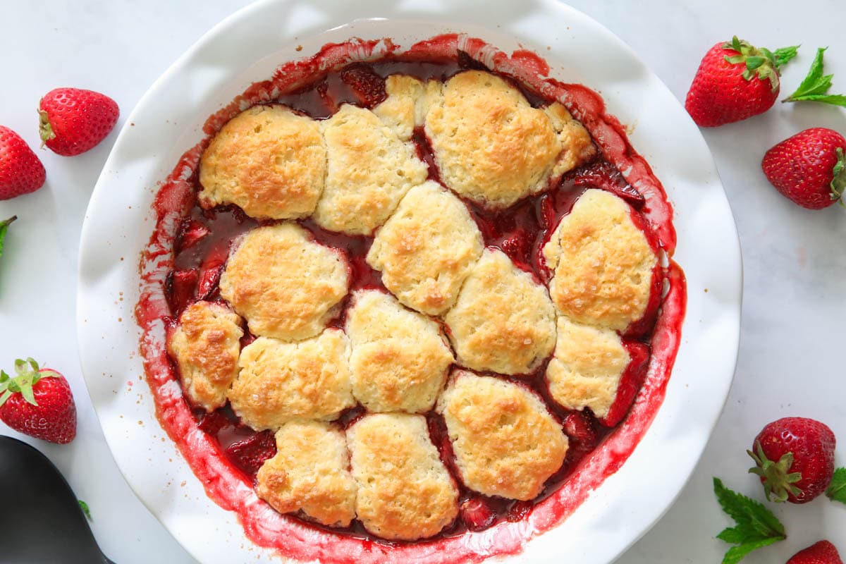 Strawberry Cobbler in a white pie dish with fresh strawberries nearby