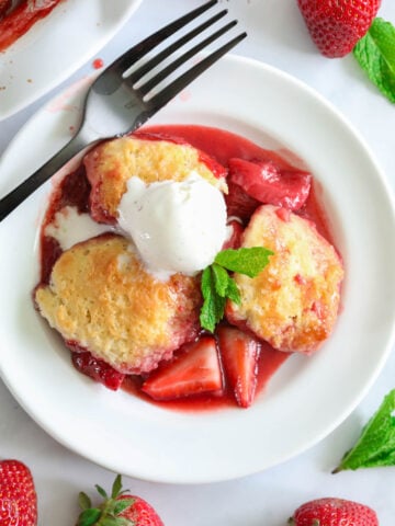 Irresistible Strawberry Cobbler served with ice cream on a pristine white plate, garnished with a fork and fresh strawberries.