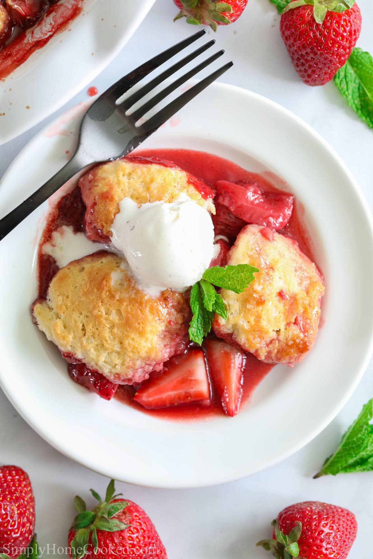 Strawberry Cobbler with ice cream on a white plate with a fork and strawberries nearby
