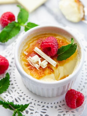 White Chocolate Creme Brulee in a ramekin and topped with white chocolate shavings, mint leaf, and raspberries.