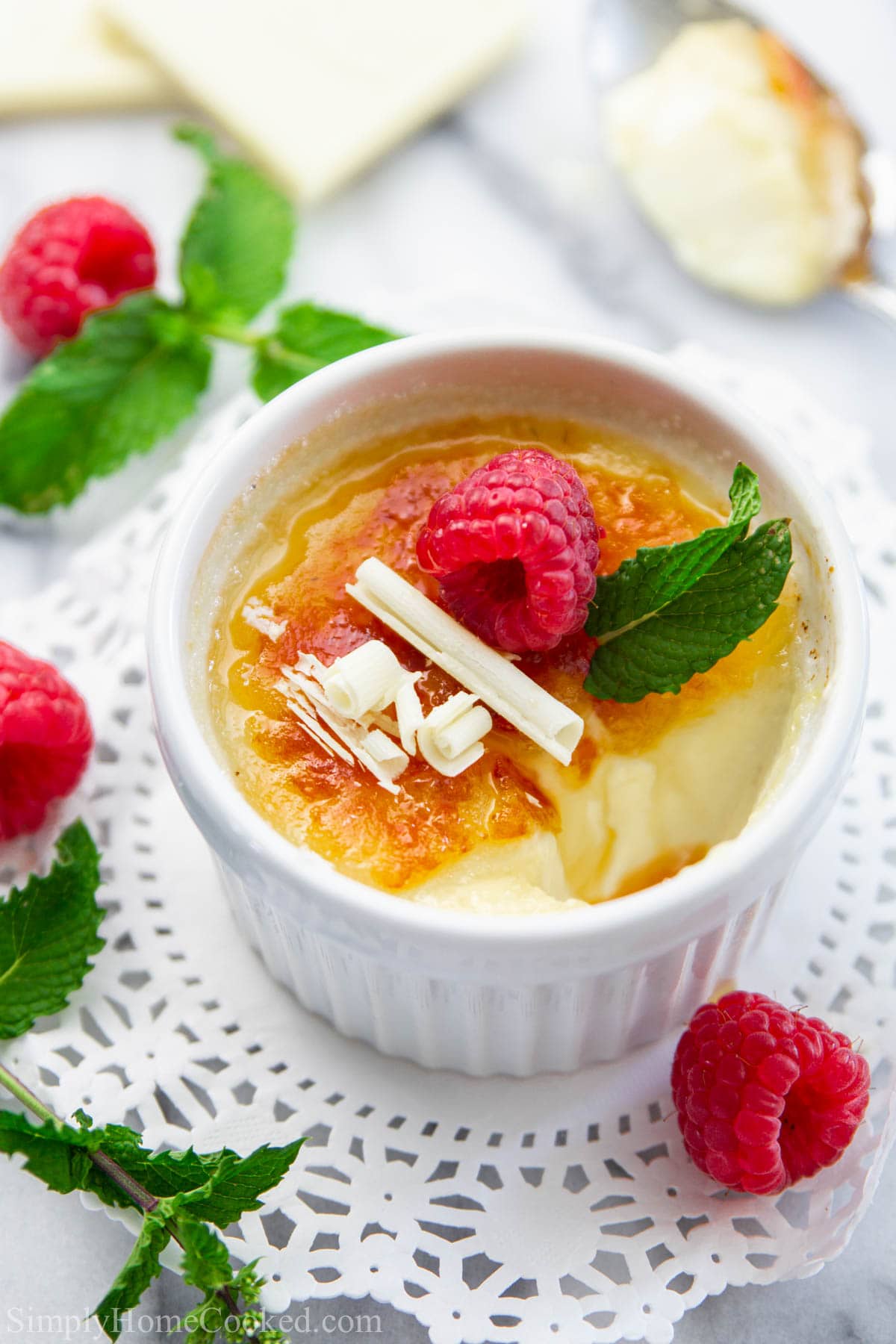 White Chocolate Creme Brulee in a ramekin and topped with white chocolate shavings, mint leaf, and raspberries