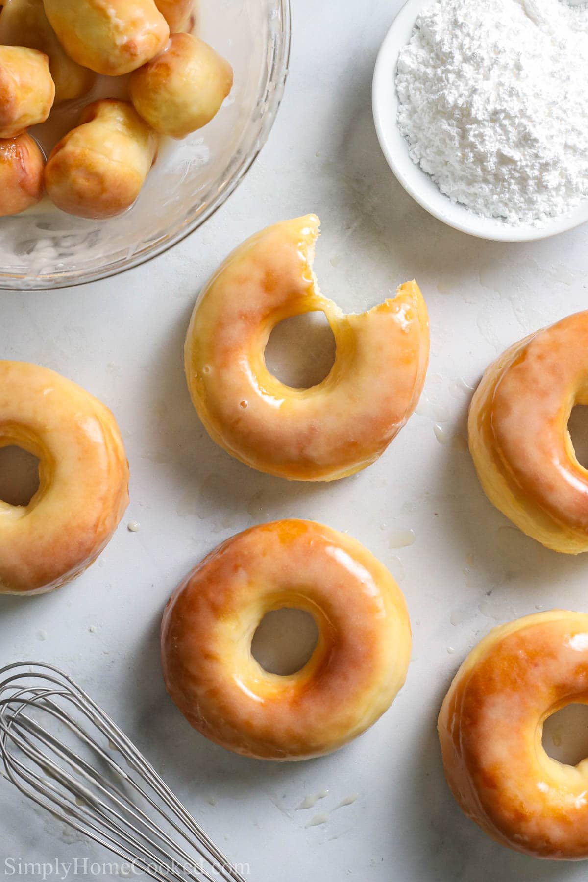 Glazed Air Fryer Donuts with donut holes, a whisk, and powdered sugar nearby.