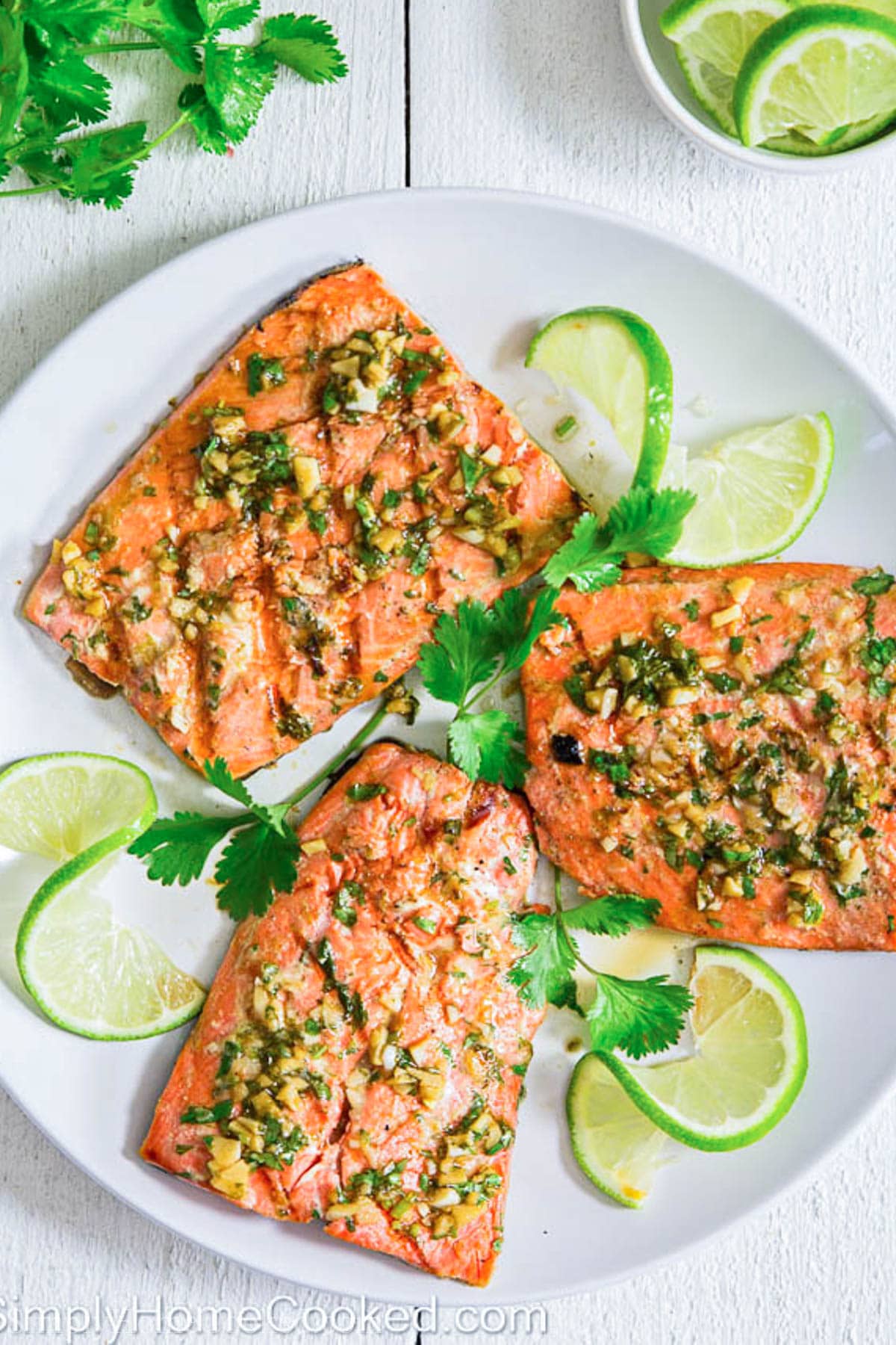 Cilantro Lime Salmon covered in marinade and on a white plate with lime slices and cilantro.
