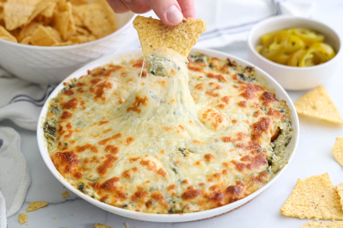 tortilla chip being dipped in cheesy hot artichoke dip. 