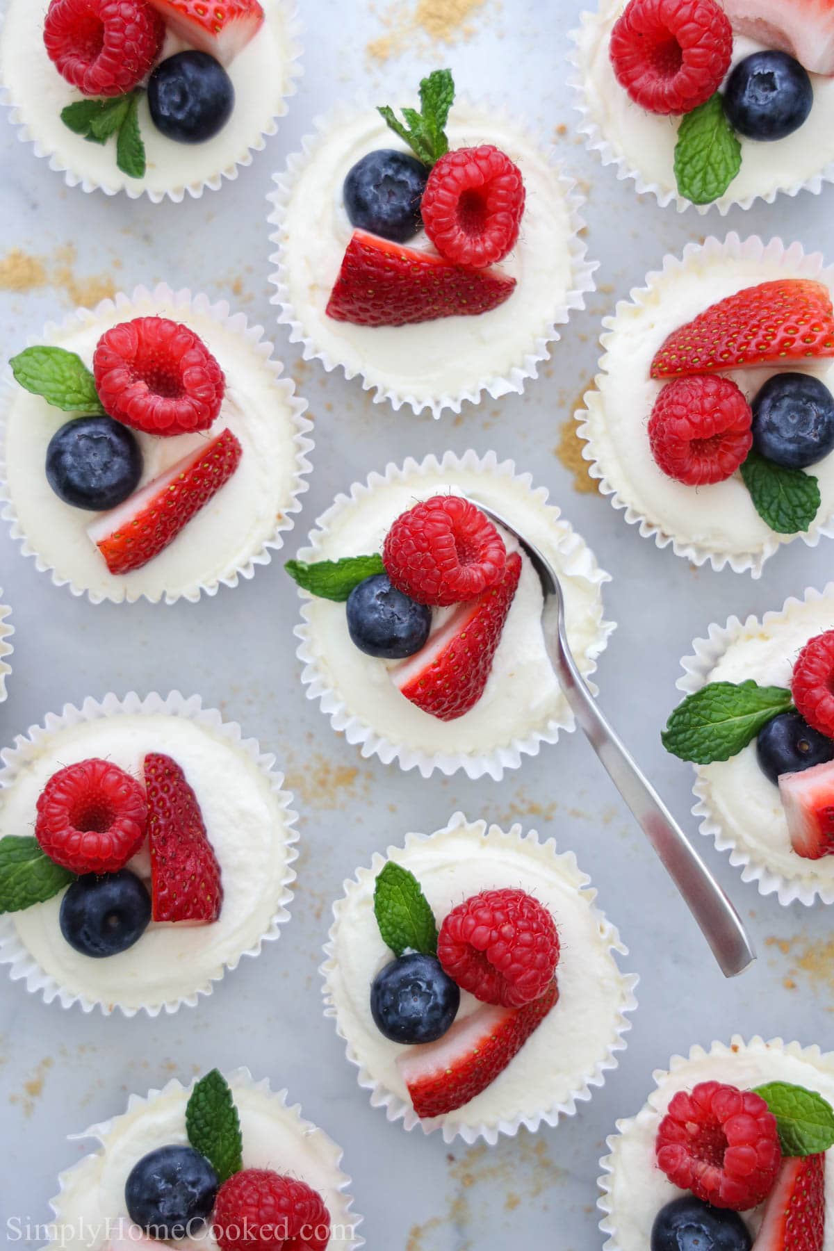 Overhead of No Bake Mini Cheesecakes topped with fresh berries and a spoon scooping into one of them