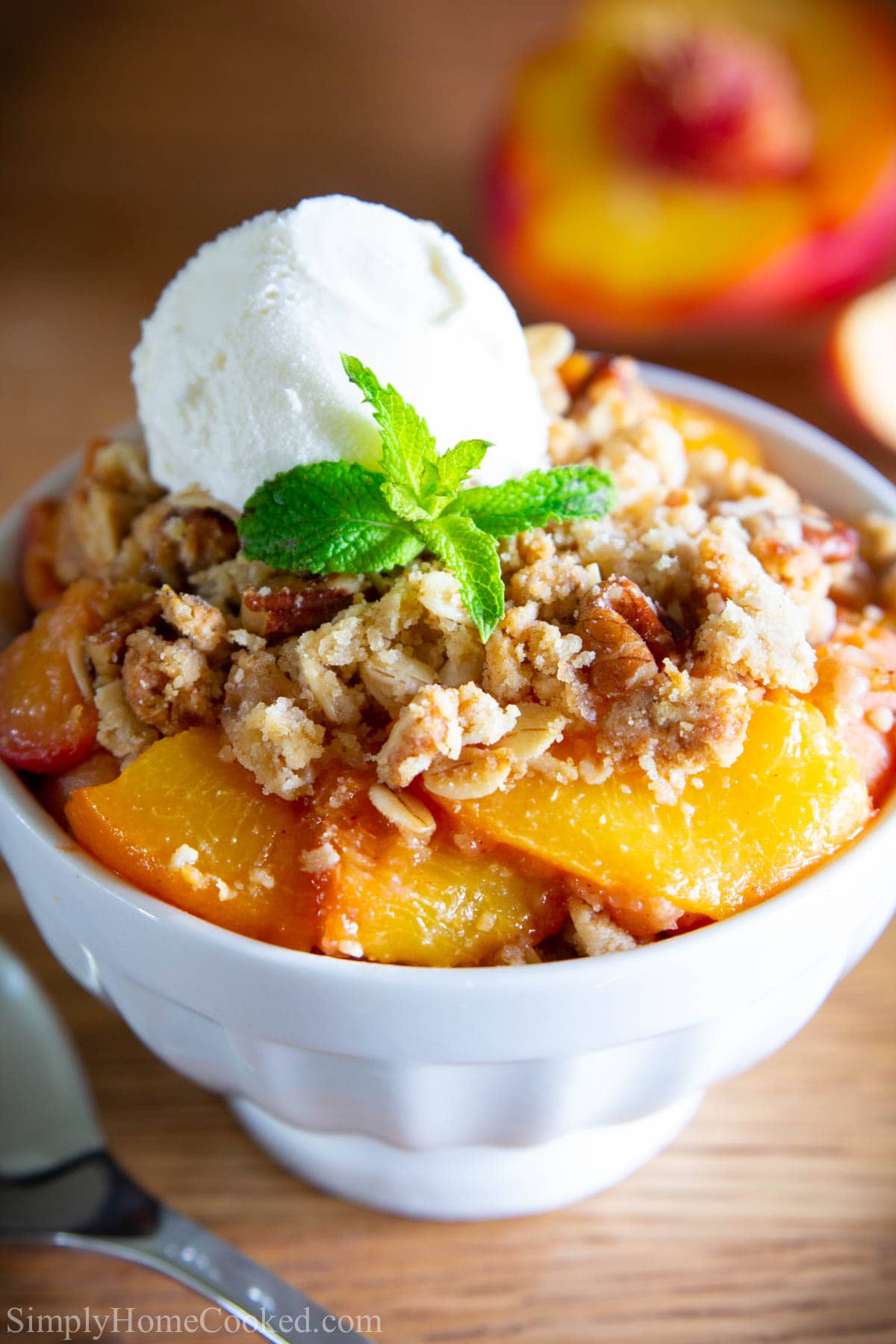 Peach Crisp in a white bowl with a scoop of vanilla ice cream on top with a mint leaf
