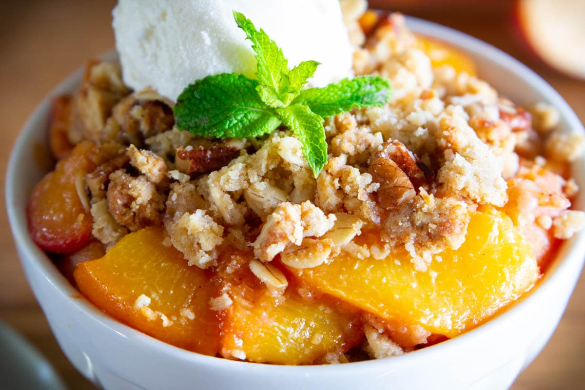 Peach Crisp in a white bowl and topped with ice cream and mint leaves.
