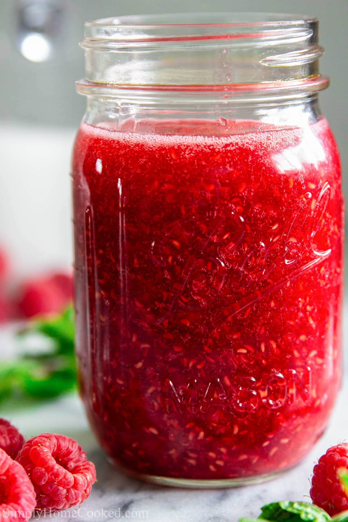 Mason jar full of Raspberry Sauce with fresh raspberries nearby