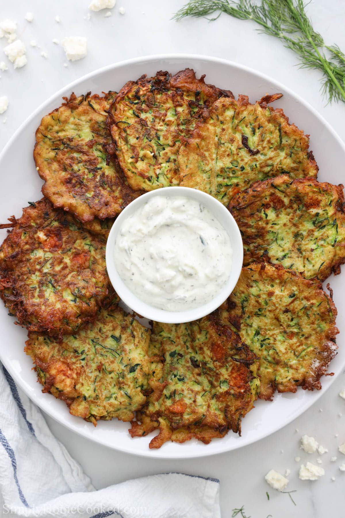 Zucchini are surrounded by a bowl of tzatziki sauce on a white plate