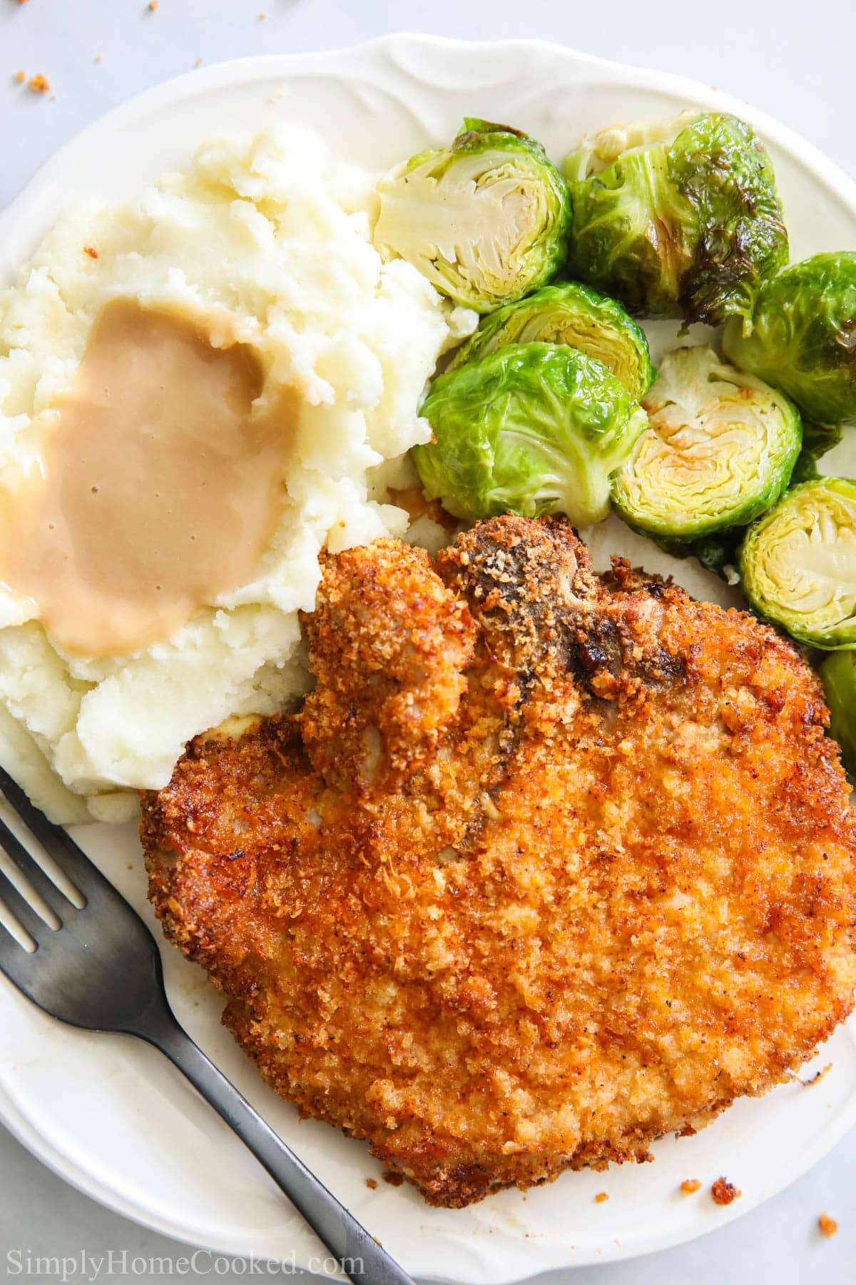 Plate of Air Fryer Pork Chops with mashed potatoes, brussels sprouts, and a fork