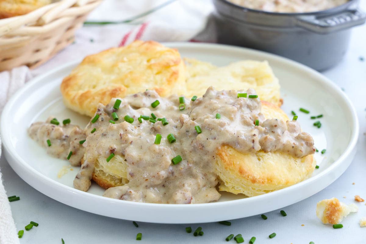 Homemade Biscuits and Gravy on a white plate with chopped chives on top.