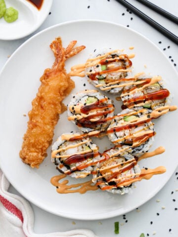 Sliced Dynamite Roll with unagi sauce and spicy mayo drizzled on top next to some shrimp tempura