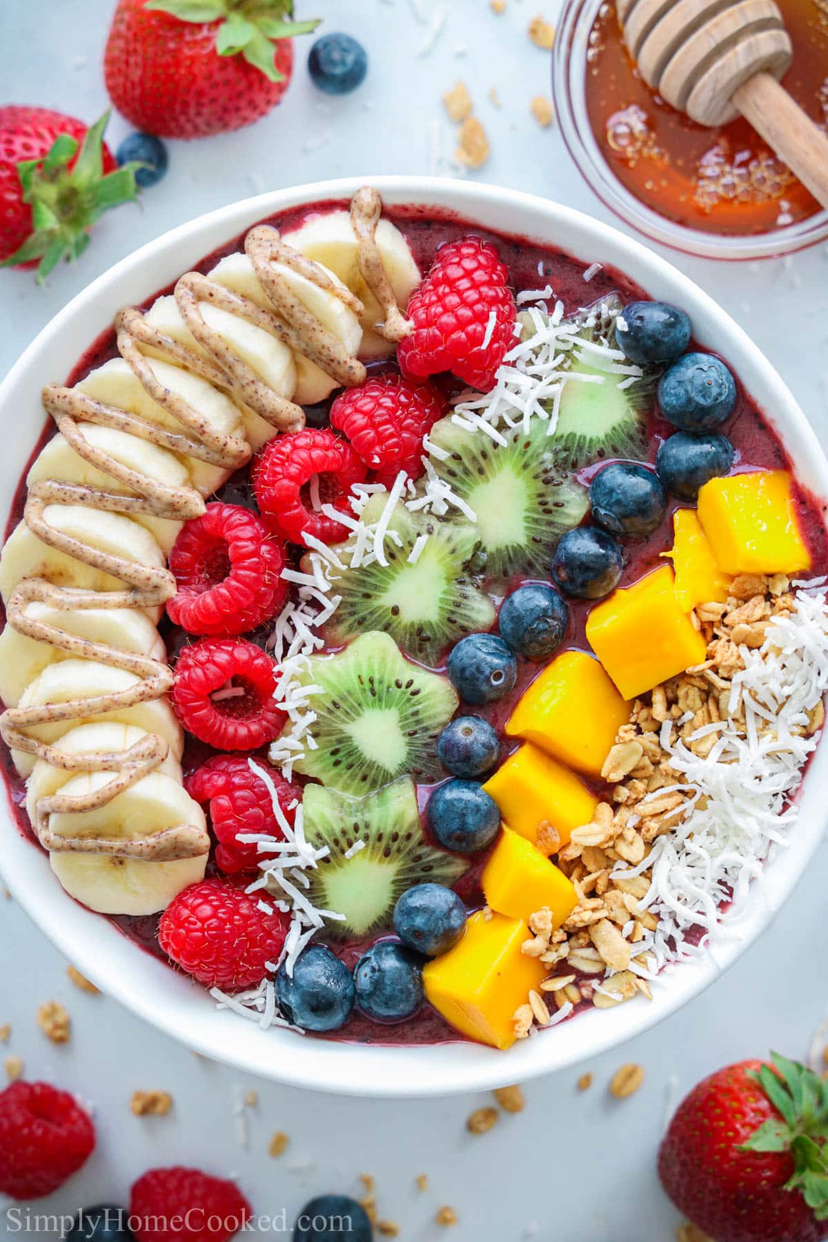 Acai Bowl topped with fresh fruit, coconut flakes, granola, honey, and nut butter, with strawberries and honey nearby.