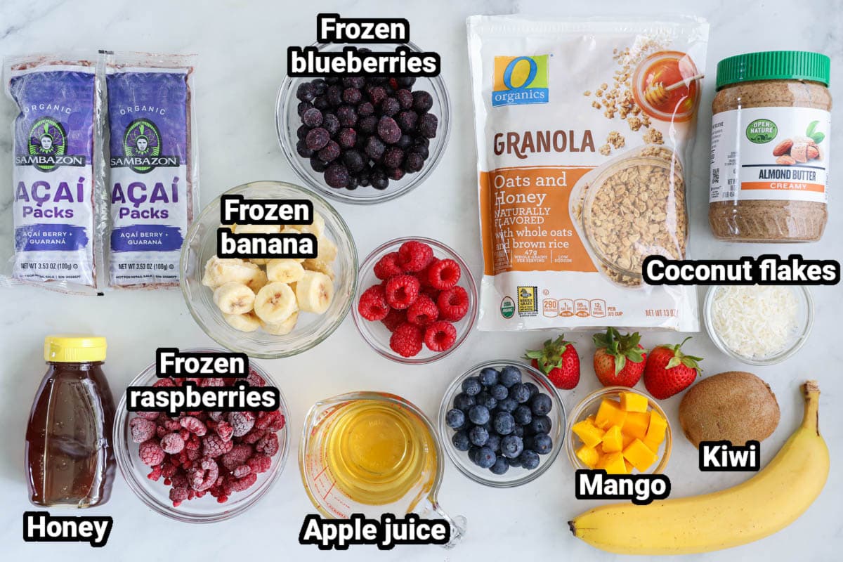 Ingredients for Acai Bowl Recipe: acai packs, frozen bananas, frozen raspberries, frozen blueberries, apple juice, bananas, blueberries, raspberries, kiwi, mango, granola, unsweetened coconut, honey, and almond butter.
