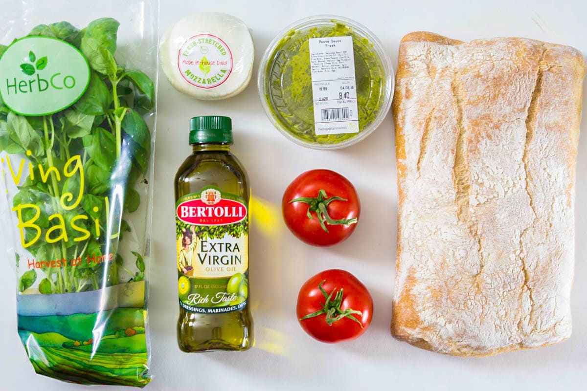 Ingredients for Caprese Sandwich: ciabatta bread, basil, olive oil, tomatoes, mozzarella, and basil pesto.