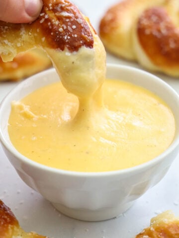 Hand dipping a piece of soft pretzel into a bowl of Pretzel Cheese Dip.