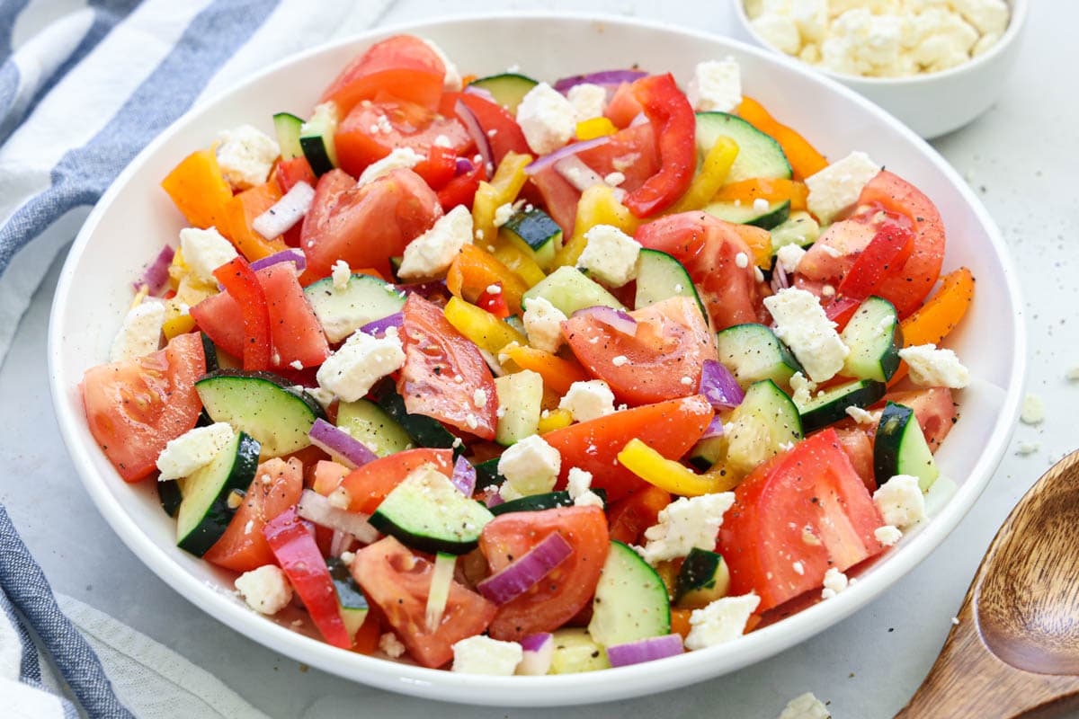 Cucumber Tomato Feta Salad on a white plate with a wooden spoon nearby
