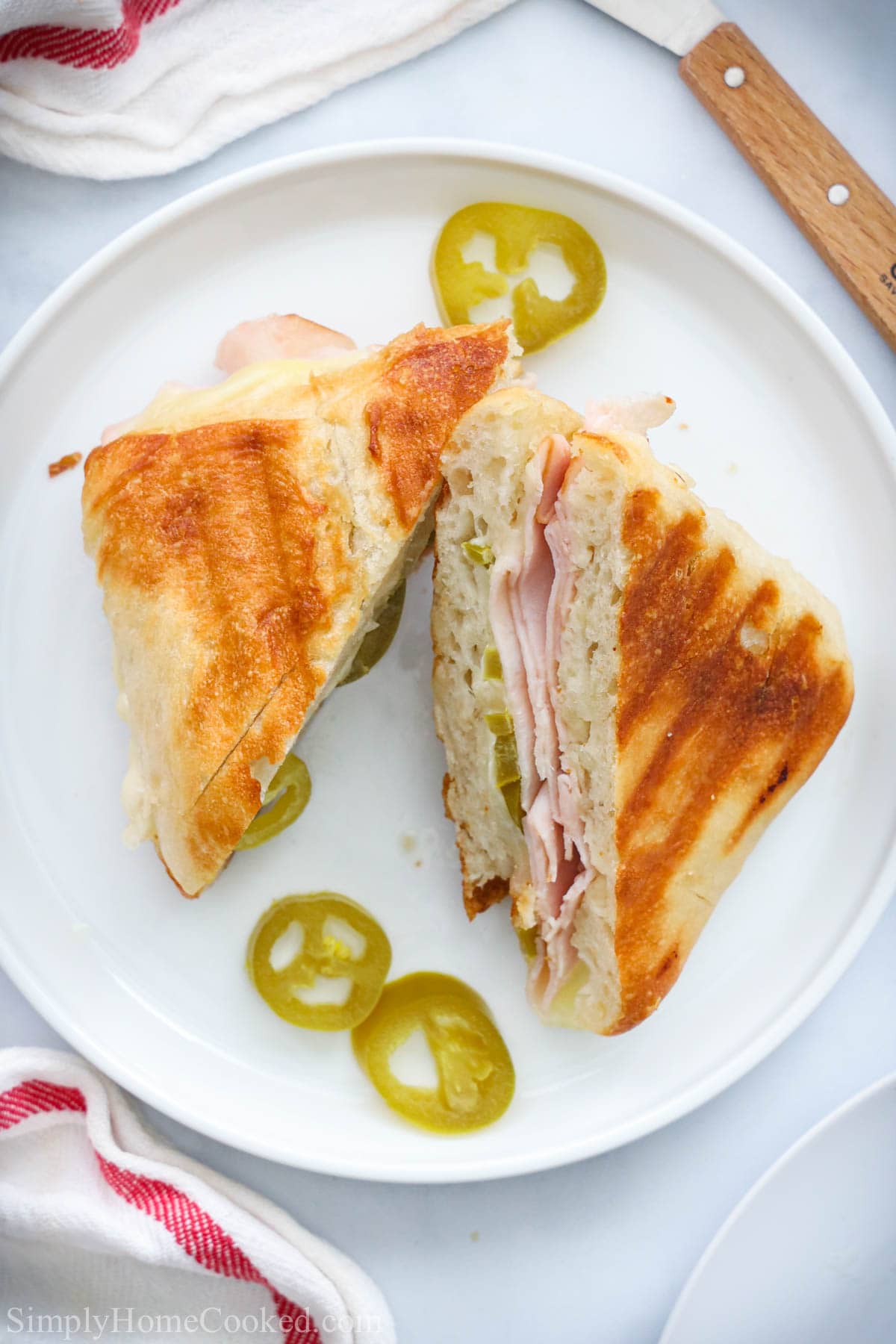 Overhead view of Turkey Panini sliced in half on a white plate with jalapeno slices.
