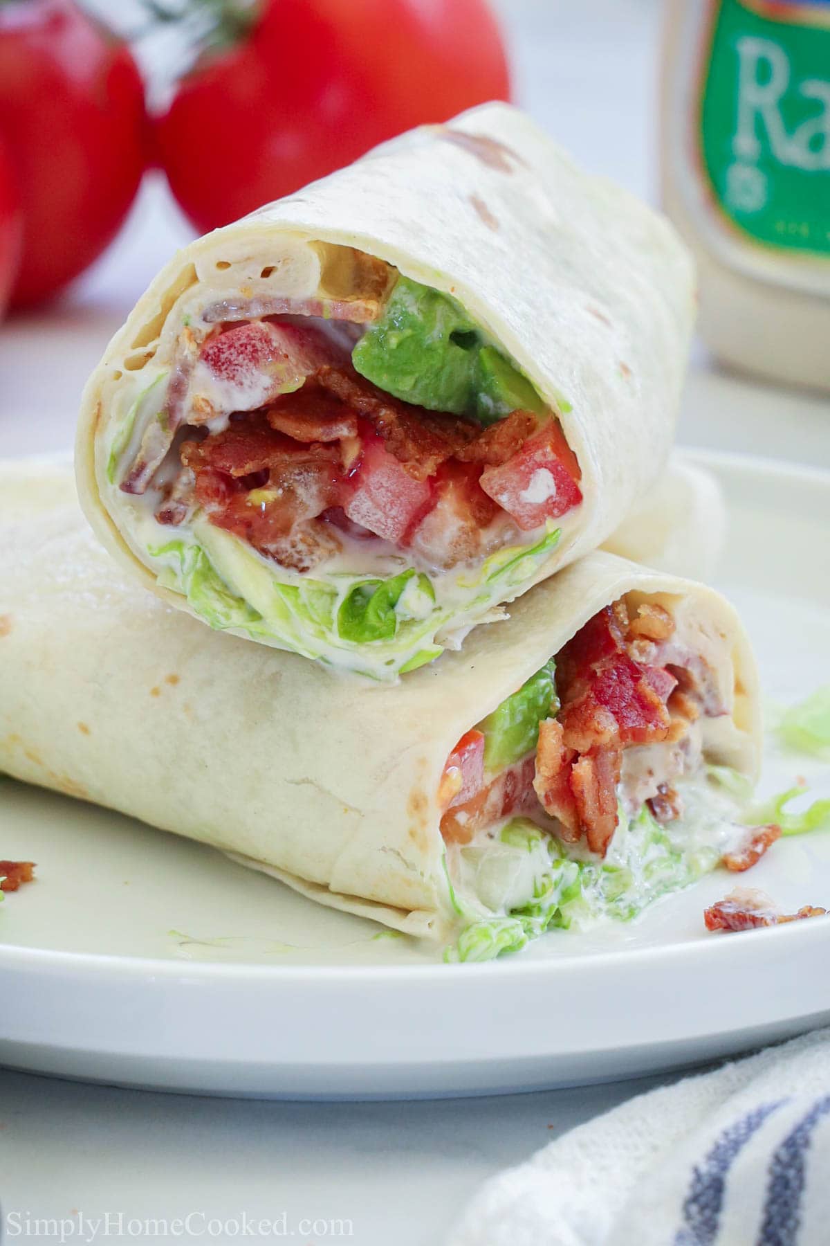 Two halves of an Easy BLT Wrap laying crosswise on top of each other on a white plate.