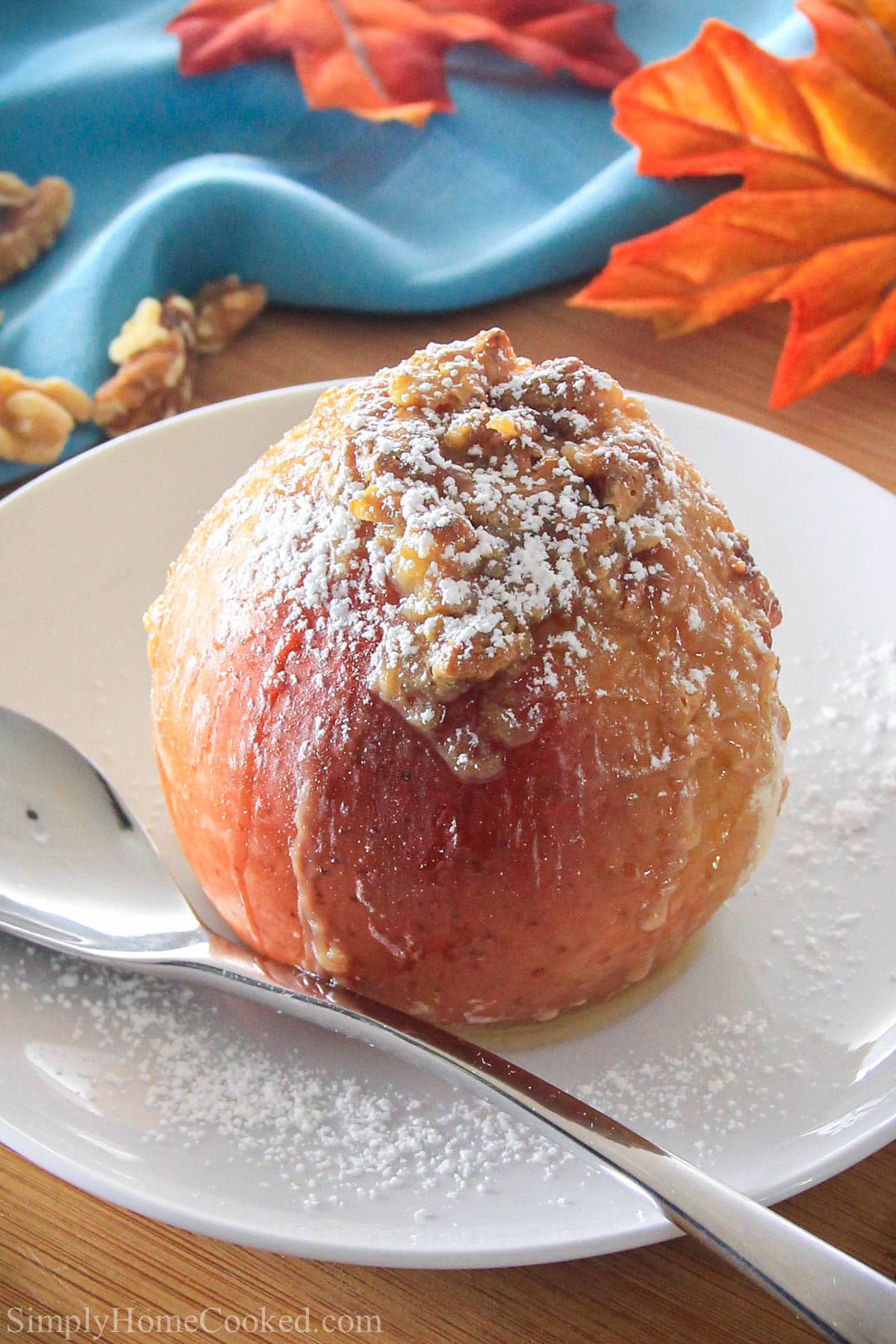 Baked Apple on a white plate covered with powdered sugar with a spoon.